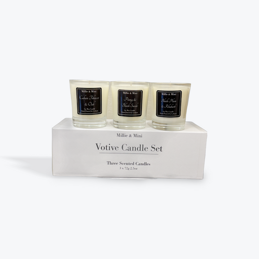 Three scented candles in glass containers on a white box labeled 'Millie & Mini Votive Candle Set' with black labels.